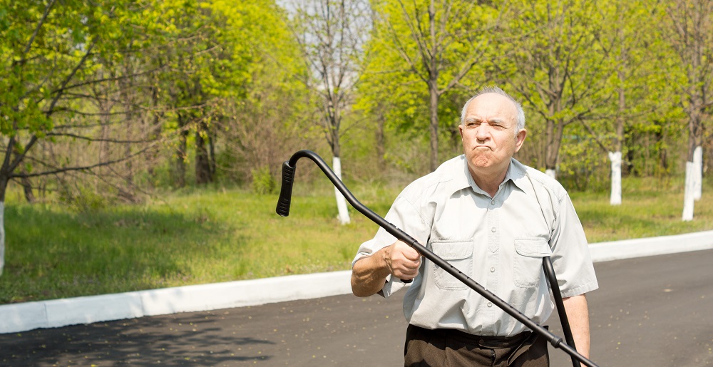 Grandparents standing in a rural street bordered by woodland waving his crutch in the air